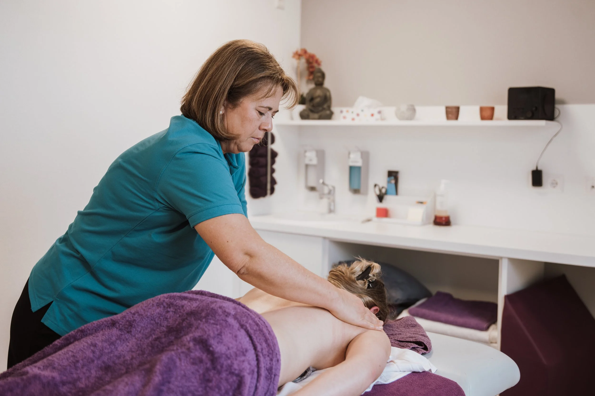 Eine Masseurin gibt einer Person eine Rückenmassage in einem Behandlungsraum.
