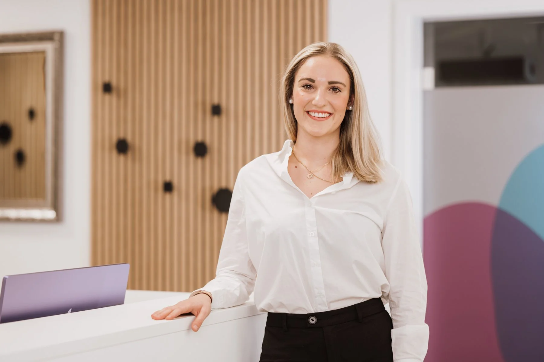 Ein lächelnde Frau steht an der Rezeption eines Hotels oder einer Dienstleistungsstelle.