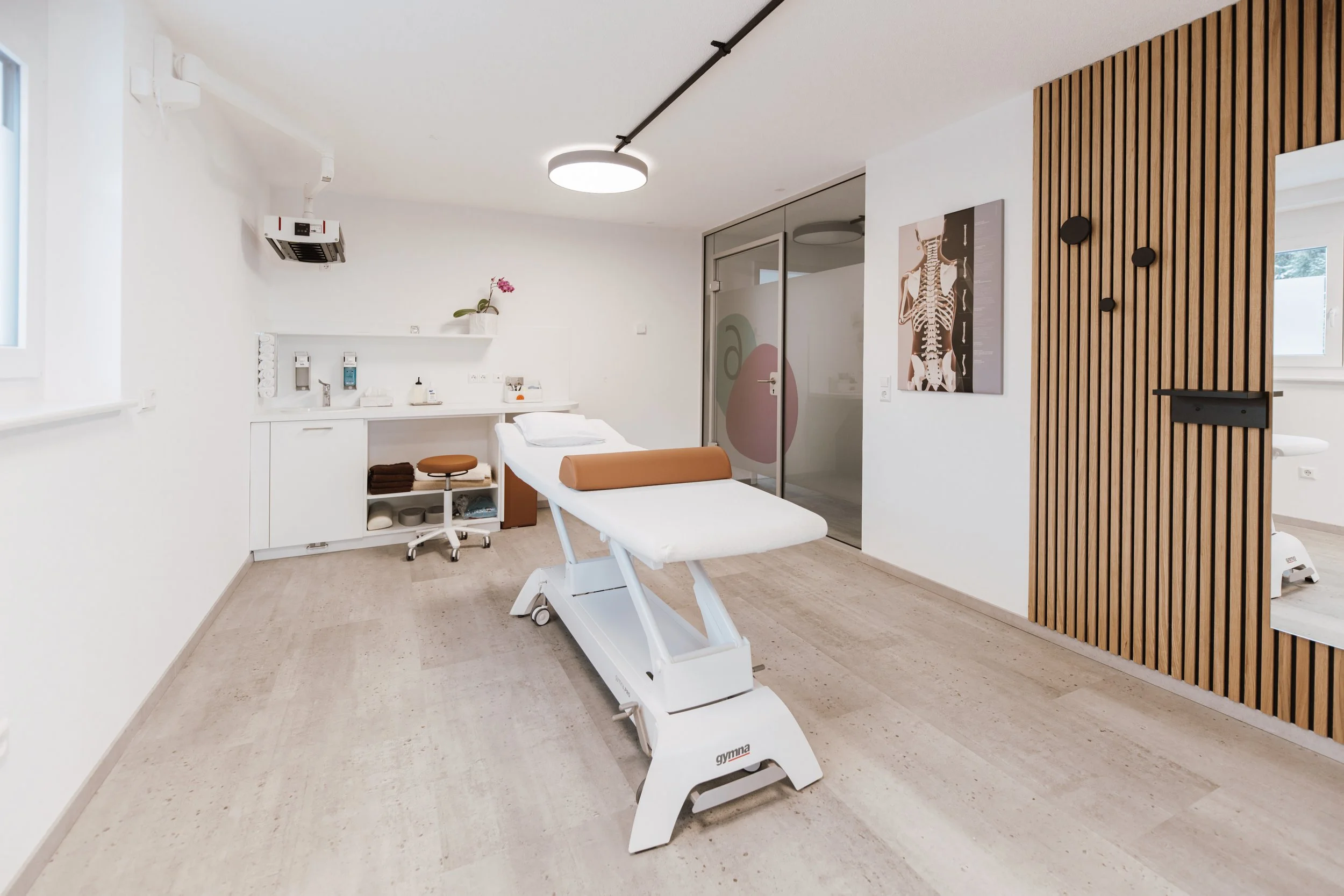 Beatmungs- oder Untersuchungsraum in einer medizinischen Einrichtung, mit Untersuchungsliege, medizinischen Geräten und Wanddekorationen.