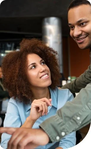 A woman and a man are engaged in a conversation at a bar or restaurant, with the woman smiling and the man leaning in towards her