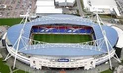 An aerial view of a large outdoor sports stadium with a soccer field inside.
