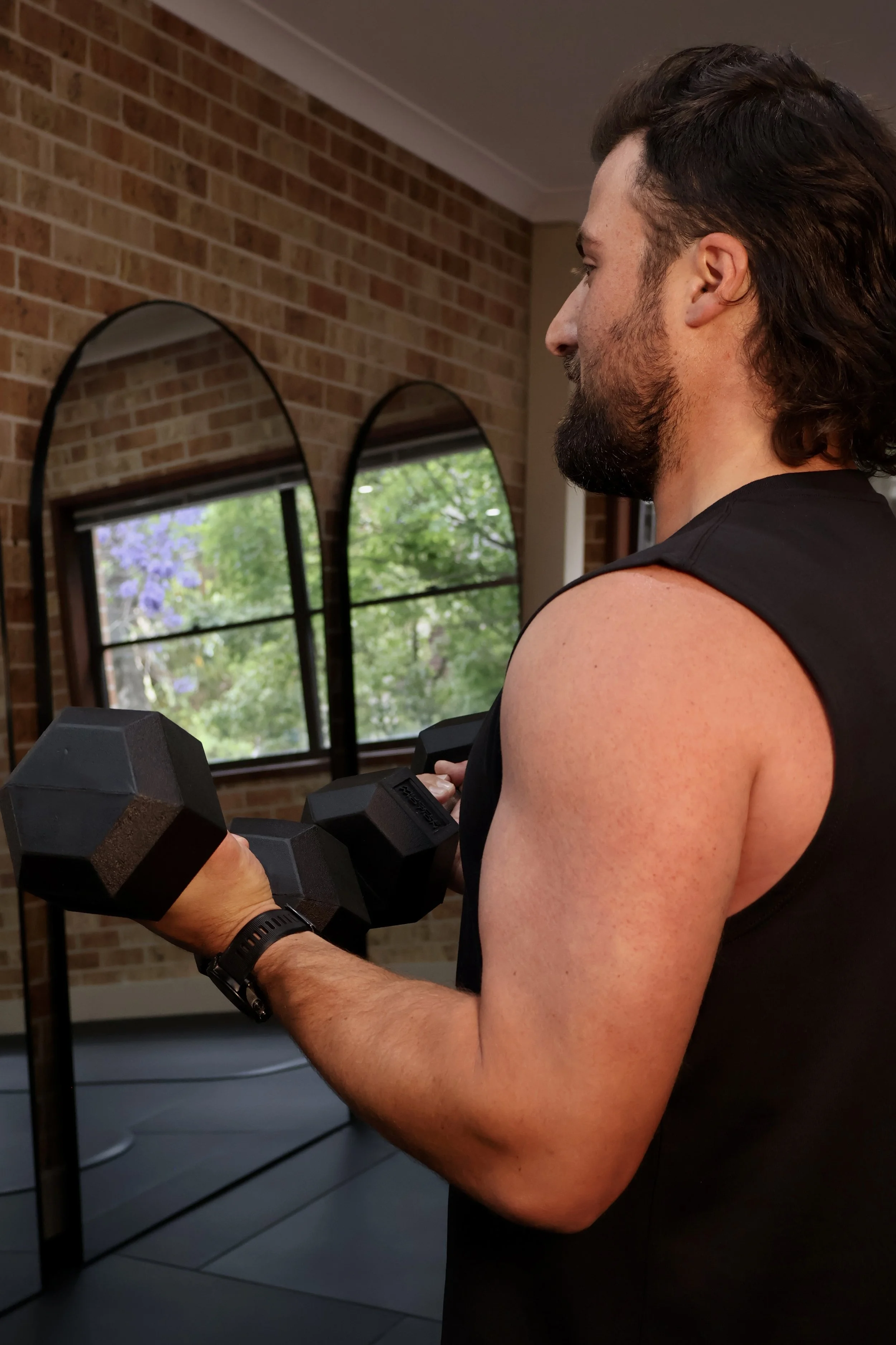 Man lifting a dumbbell in a pilates studio with brick walls and large windows