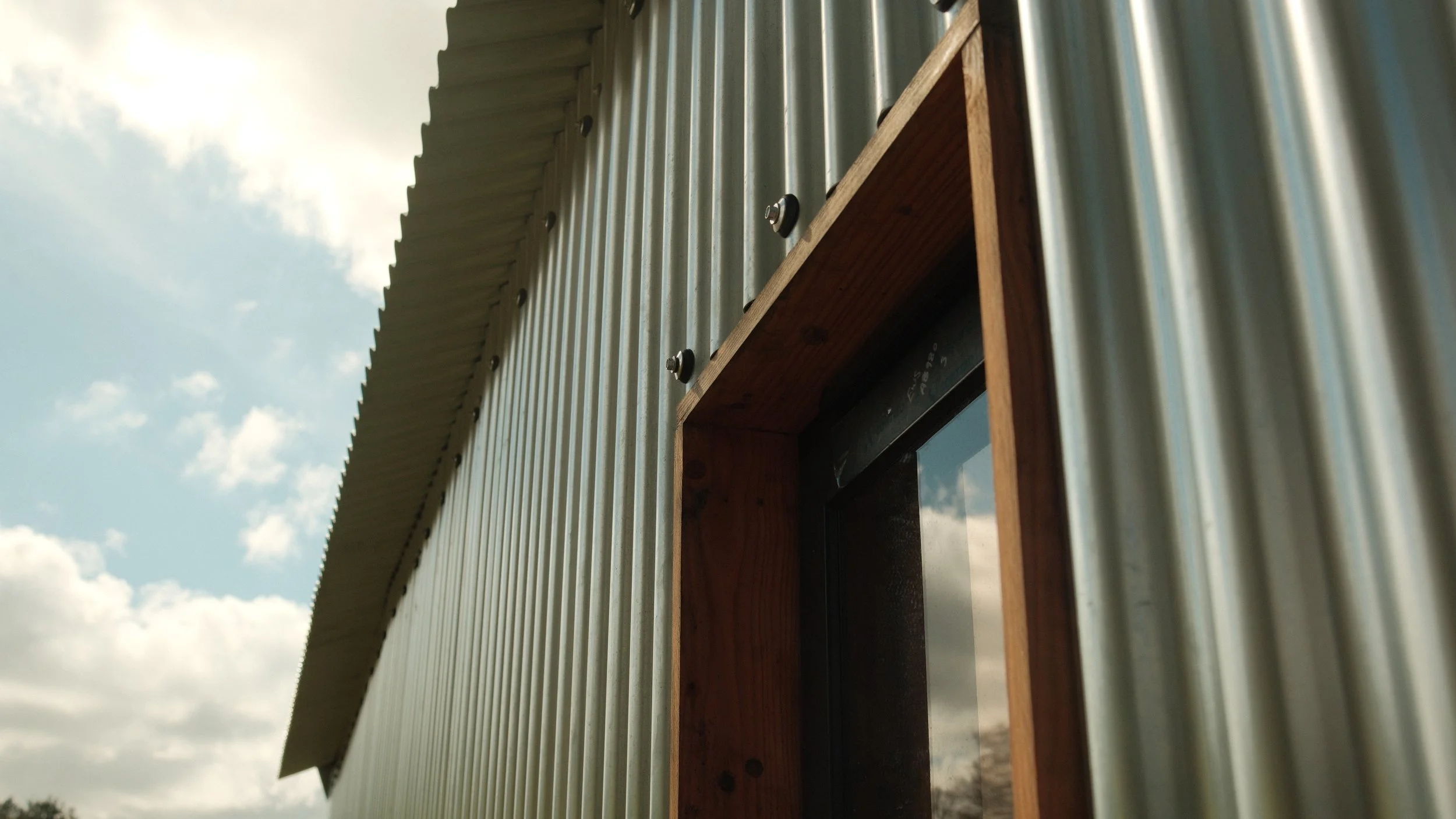Close-up of a wooden window frame mounted on a corrugated metal building against a cloudy sky.