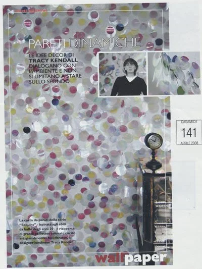 A decorative wall covered with multicolored confetti circles, with a small photograph of a woman and a floral image to the right. There is a sign with the word 'CASAMICA' and a number 141, indicating an event or exhibition. The text is in Italian, me