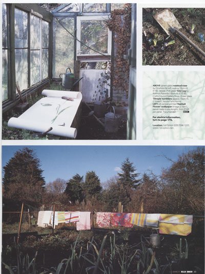 A plant nursery with a greenhouse in the top left and a clothesline with colorful laundry hanging outside in a garden, with trees in the background.