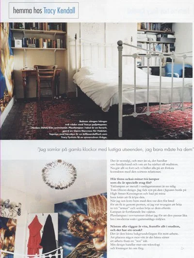 A cozy bedroom with a white metal bed, a red patterned rug, a wooden desk with a chair, and bookshelves on the walls full of books.