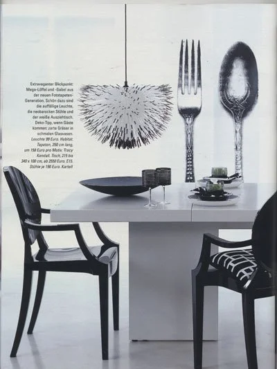 Decorative wall art featuring oversized utensils and a fur-like object, with black chairs surrounding a white dining table.