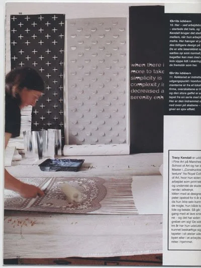 A person cleaning a rug on a table in a room with dark and patterned wall decor. There are glasses and a tablet on the table.