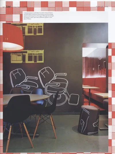 Indoor cafe or lounge area with black wall featuring white line art of chairs and electronic devices, red pendant light, yellow window frames on the wall, and seating with tables and a patterned ottoman, all framed by a red and white checkered border