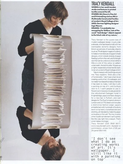 A woman with short hair looking at a tall, narrow, white sculpture made of stacked layers in a gallery setting.