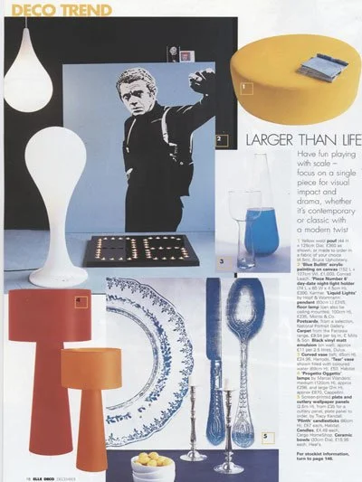 A magazine page displaying various home decor items, including a black and white poster of a man, a yellow circular table with blue books, a blue glass with a straw, a large white floor lamp, a red and orange table lamp, blue and silver cutlery, and 