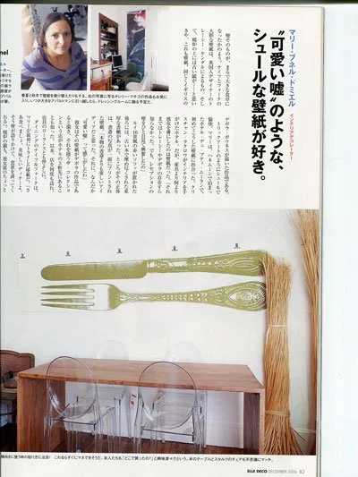 A magazine page featuring an article with Japanese text, a photo of a woman in a purple and gray striped sweater, and an image of a decorative fork and knife wall decoration above a dining table with two transparent chairs. There is also a bundle of 