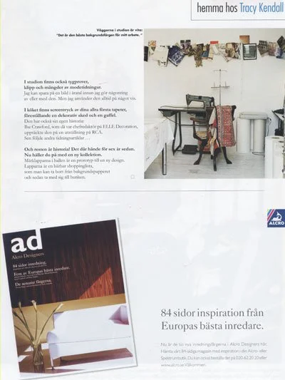 A collage of various small photographs hanging from a wire line in a bright white room. A woman sits on a chair in front of a white desk, looking away. The wall behind has a quote in Swedish.