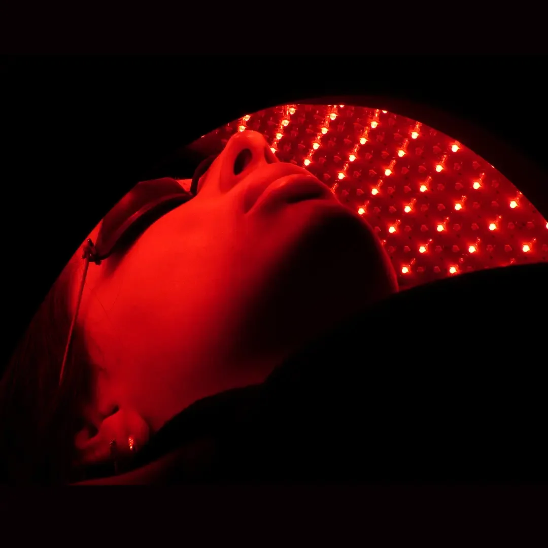 Person lying inside a red LED light therapy device, with their face illuminated by red lights.