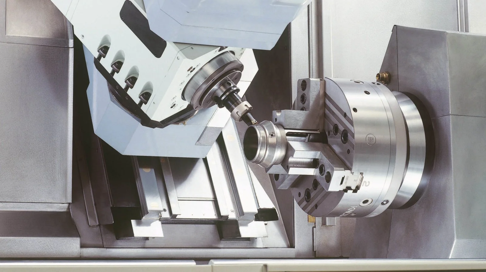 Macchina CNC con braccio meccanico e pezzo di metallo in fase di lavorazione.