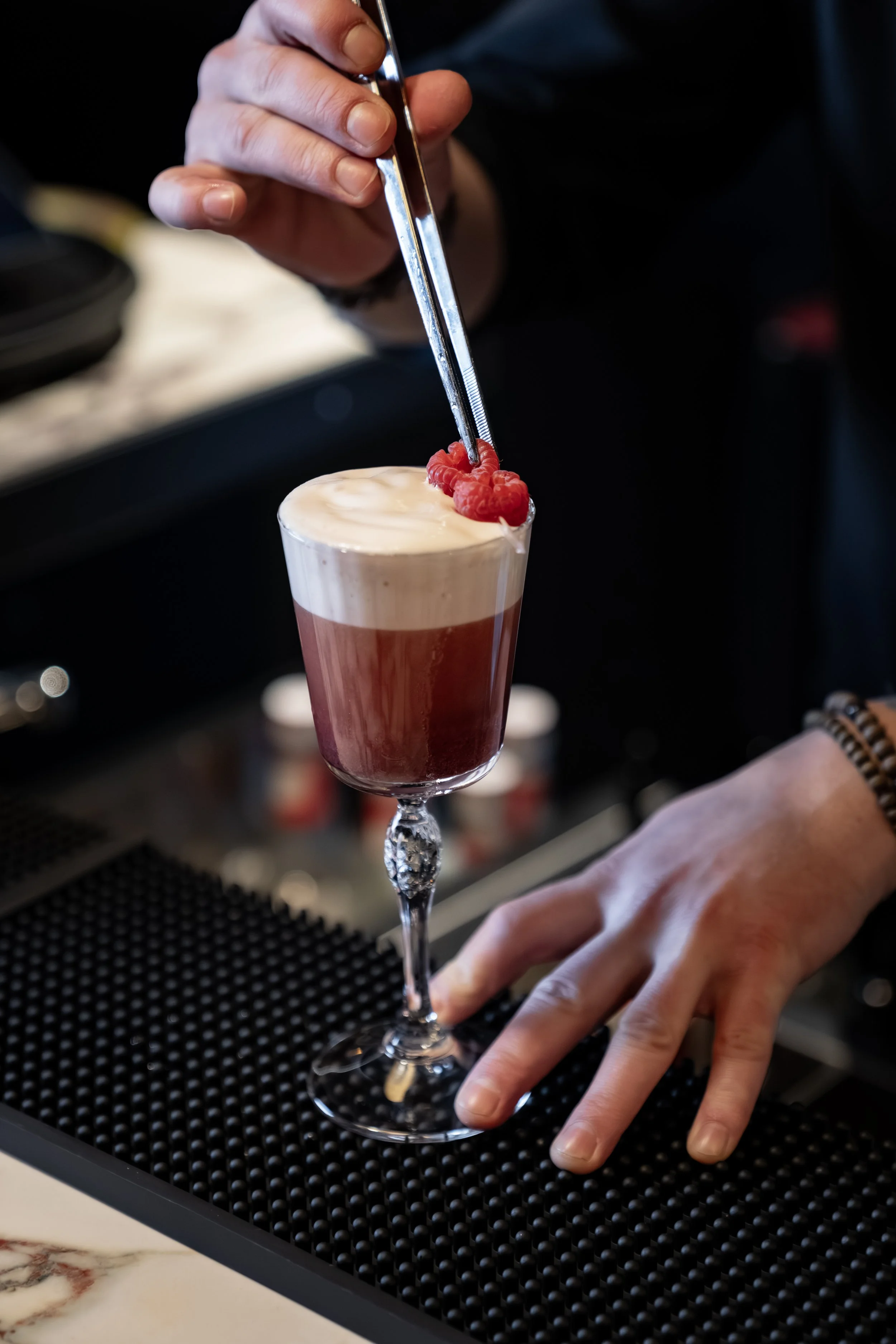 En bartender plasserer bringebær på en lagd cocktail i et elegant vinglass.