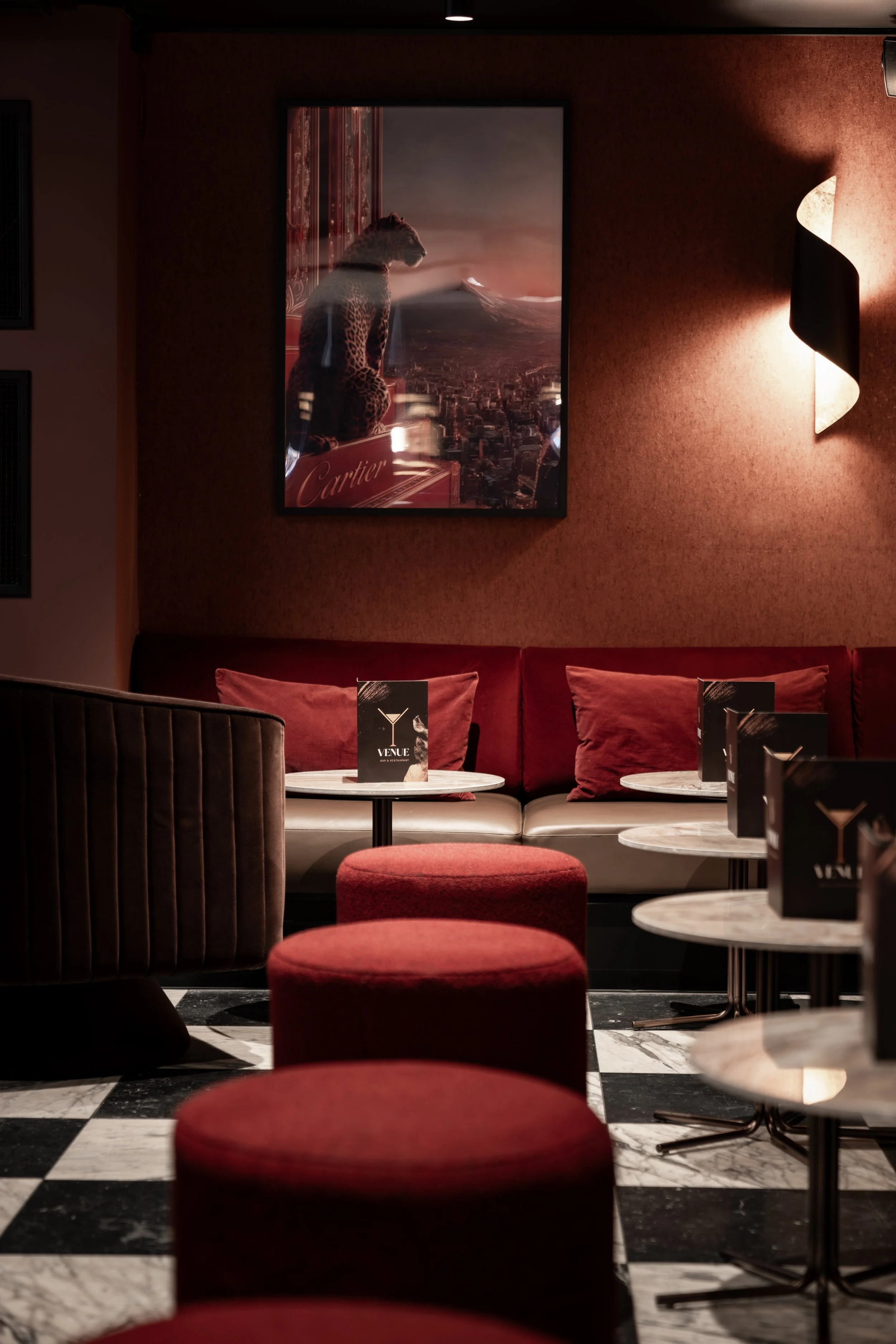 Innendørs loungeområde med røde og svarte møbler, en stor kunstplakat med en jaguar på veggen, med mørk vegg og belysning. Luksuriøs følelse, og møbler i fløyel eller velour materiale.