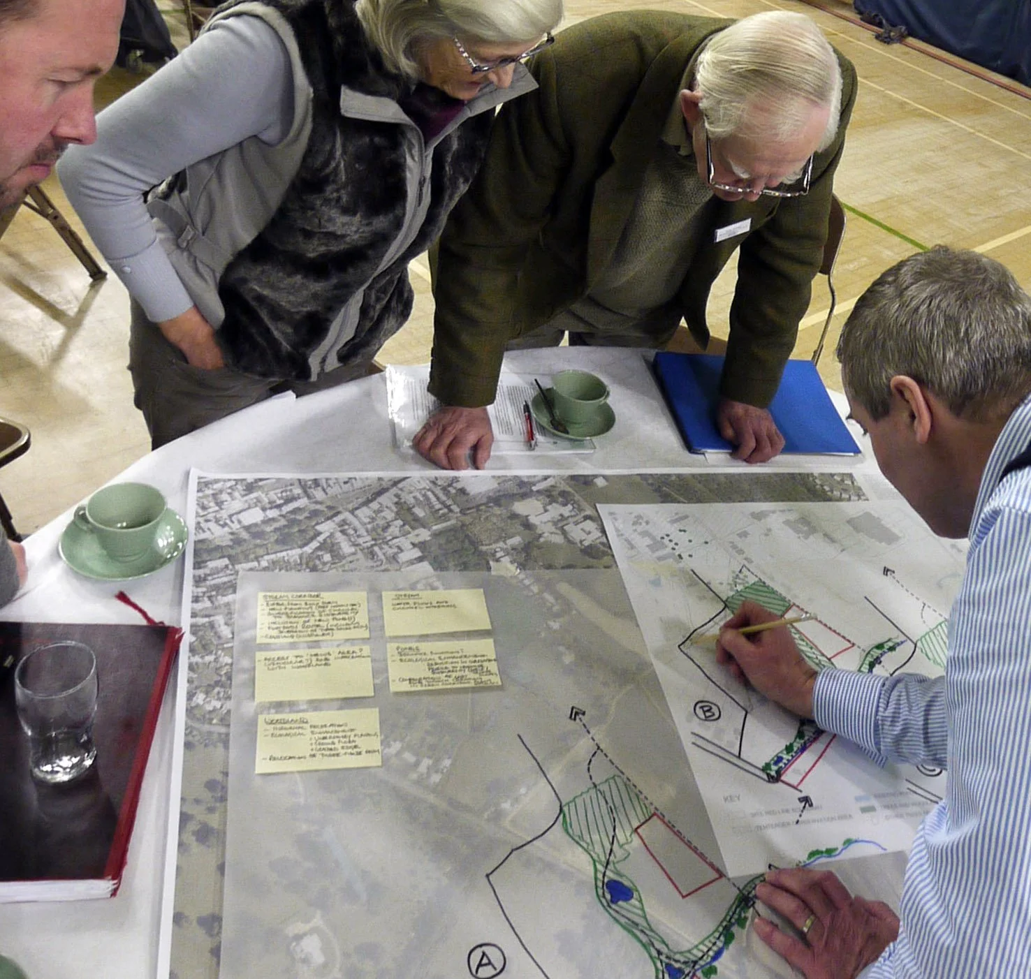 Group of people gathered around a table analyzing maps and plans for urban planning or development.