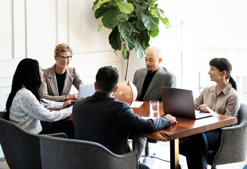 Cinq personnes en réunion autour d'une table en salle de conférence, avec un globe et des ordinateurs portables.