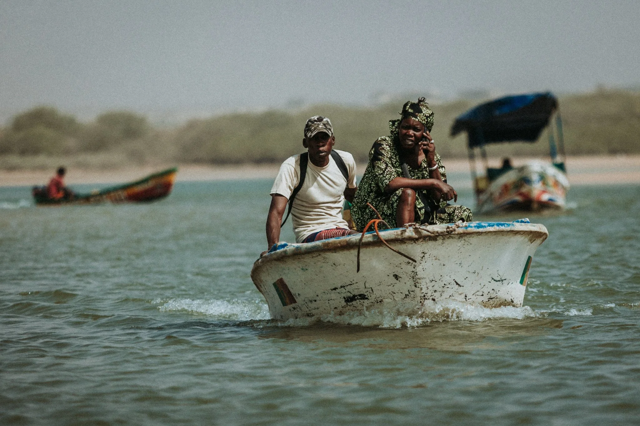 Deux personnes assises sur un bateau en mer, l'une parlant au téléphone et l'autre regardant devant eux, avec un autre bateau en arrière-plan.