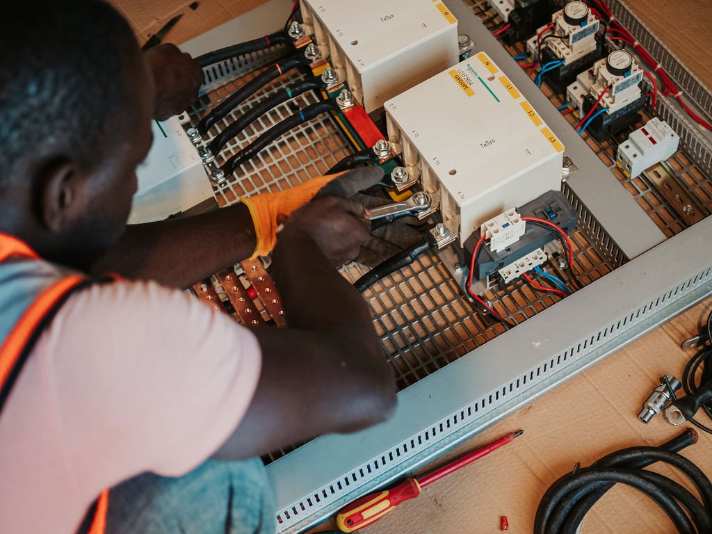 Un technicien en train d'installer ou d'entretenir un tableau électrique avec des composants électroniques et des câbles.