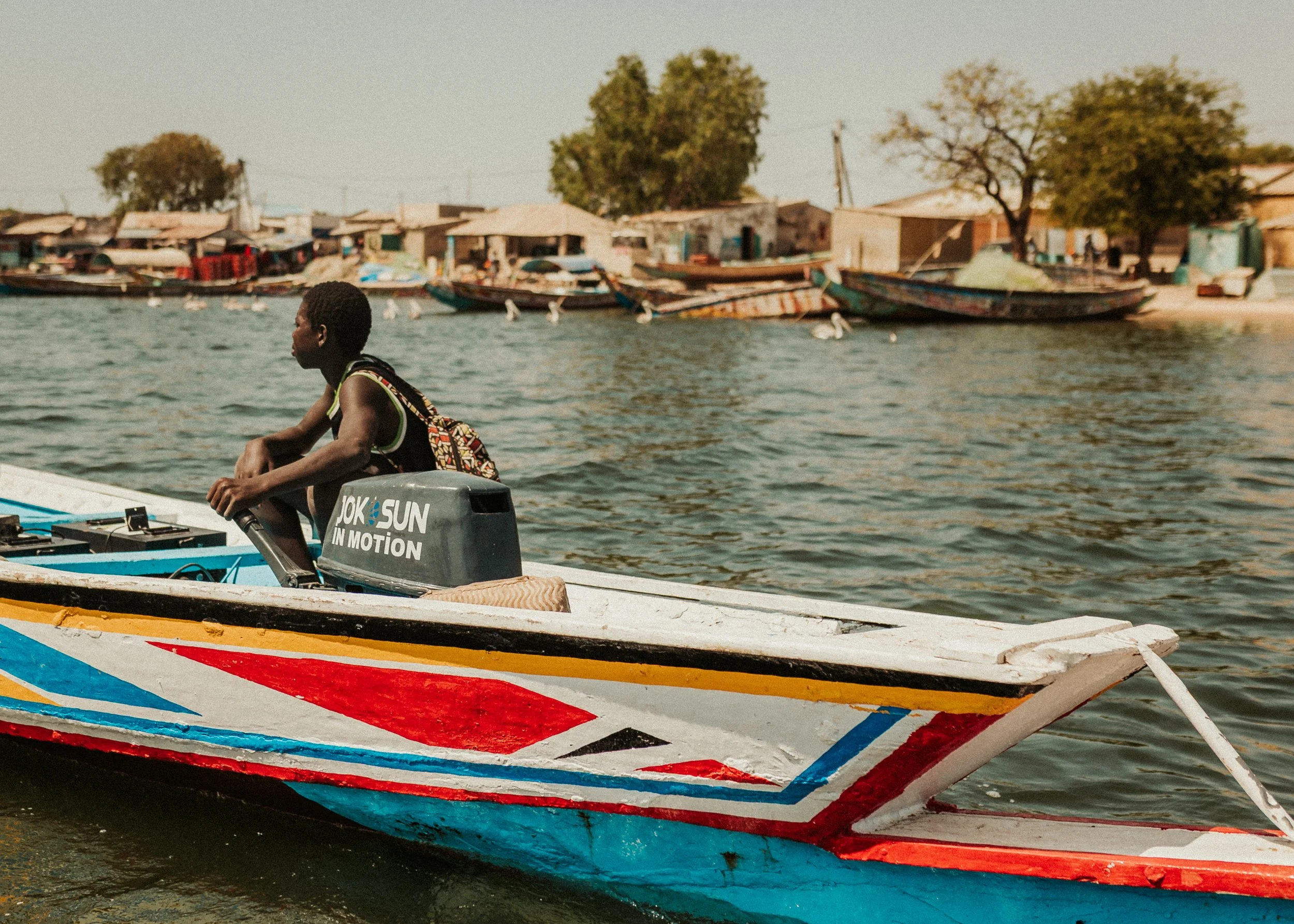 Un homme pilotant un bateau en mer près d'un village avec des maisons  et des arbres en arrière-plan.