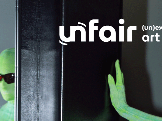 Parte di una mostra d'arte intitolata 'Unfair', con una mano verde di plastilina che tocca una superficie nera.