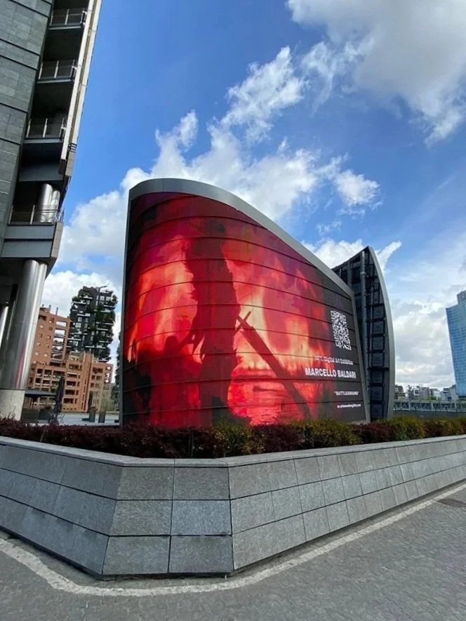 Installazione di digital art su maxi schermo a Milano, con figura guerriera in silhouette esposta su facciata architettonica contemporanea.