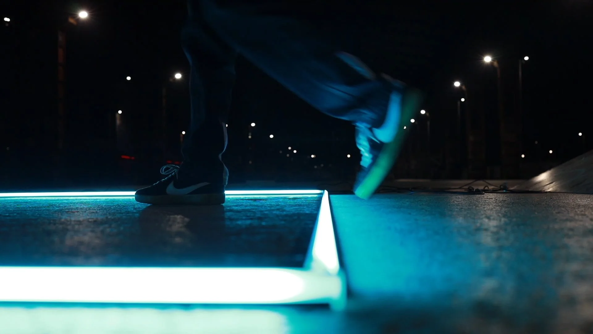 Artista VR in movimento su una superficie illuminata da luci al led blu, con lampioni accesi sullo sfondo durante la notte.