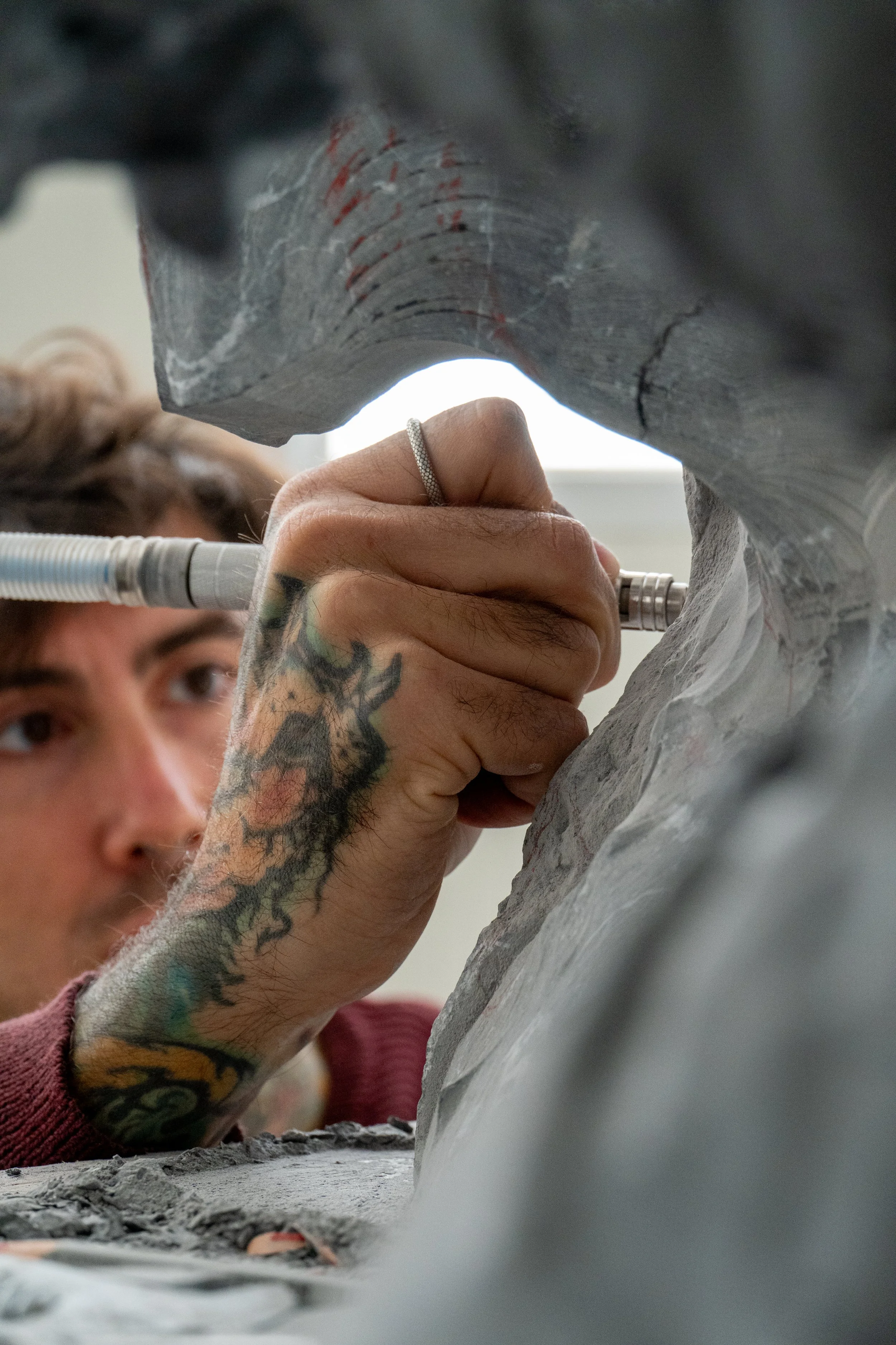 L'artista Marcello Baldari con tatuaggi sta scolpendo una scultura in marmo, concentrata sul lavoro.