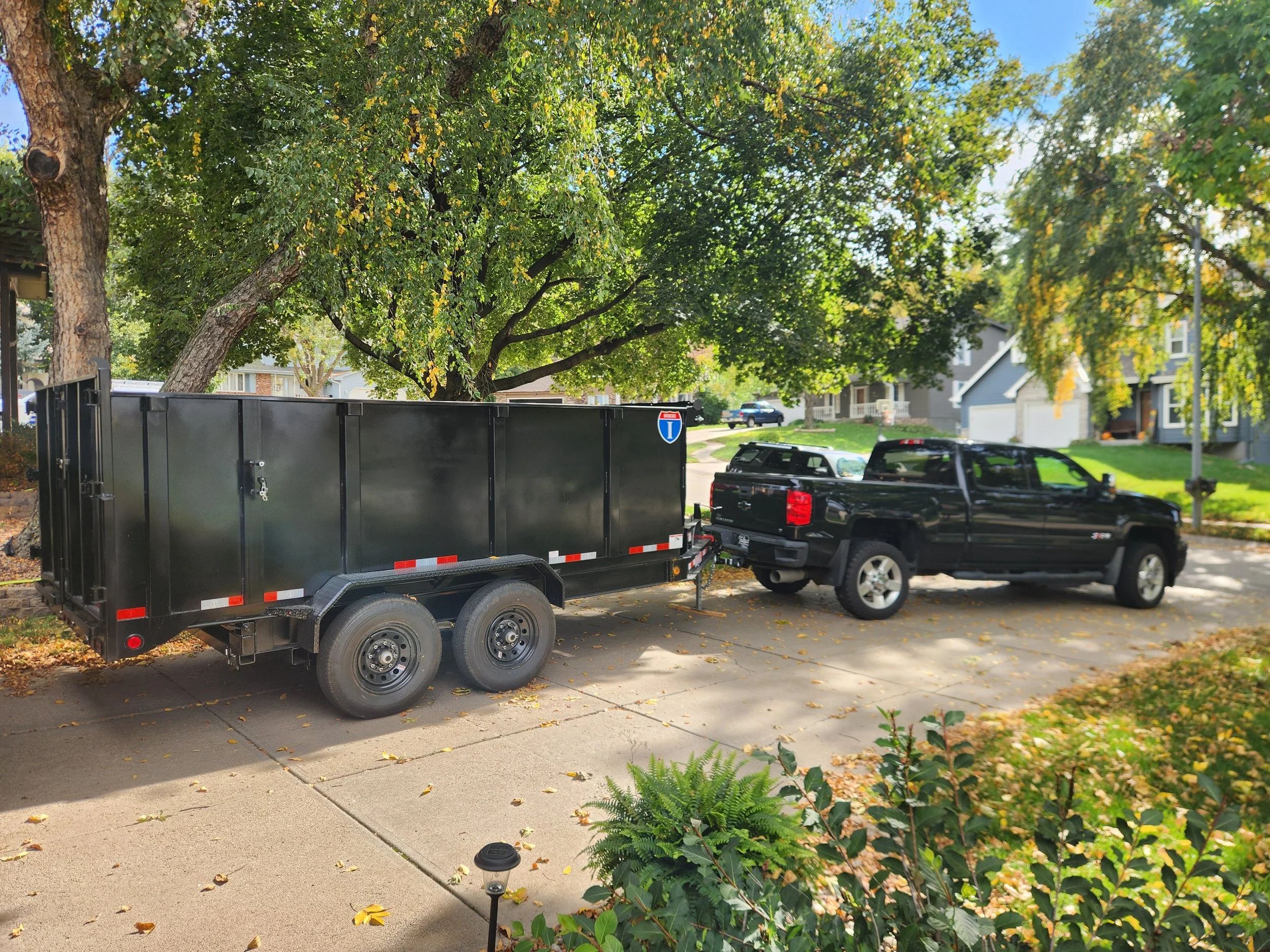 Black pickup truck towing a black enclosed junk removal trailer parked in a residential driveway.