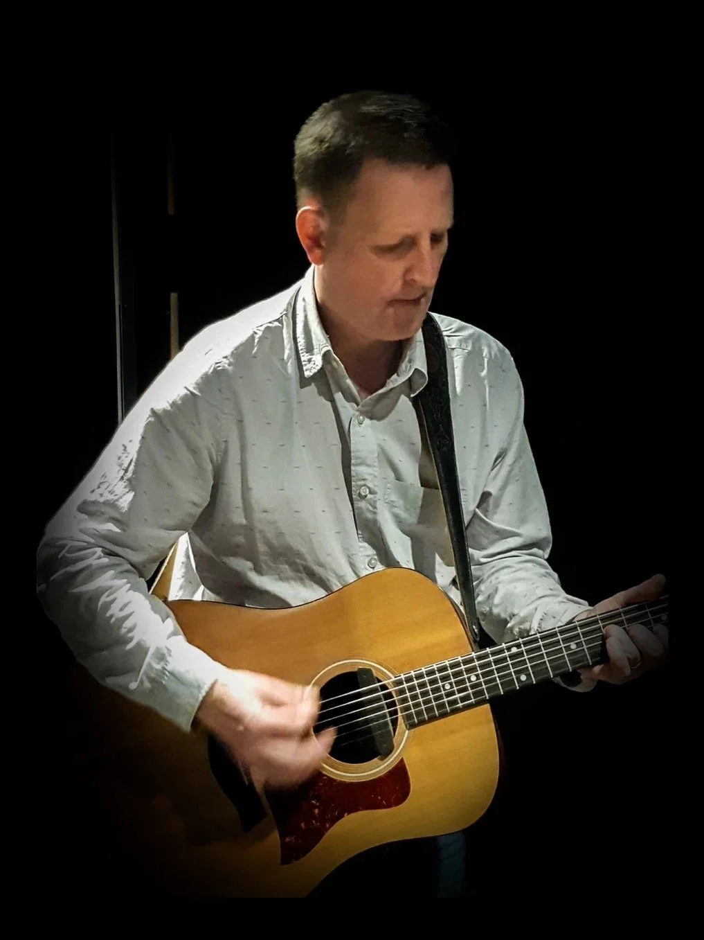 Man playing an acoustic guitar in a dark setting.