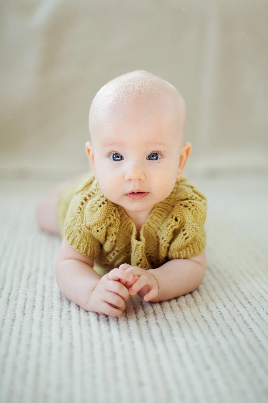 6 måneder gammel baby ligger på magen og ser inn i kamera.