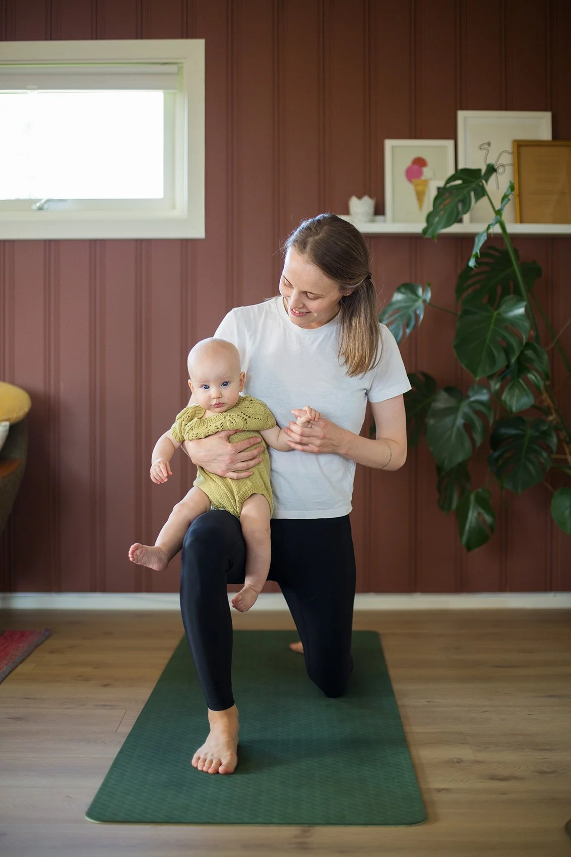 Miljøportrett av mor og baby som gjør yoga sammen på treningsmatte.