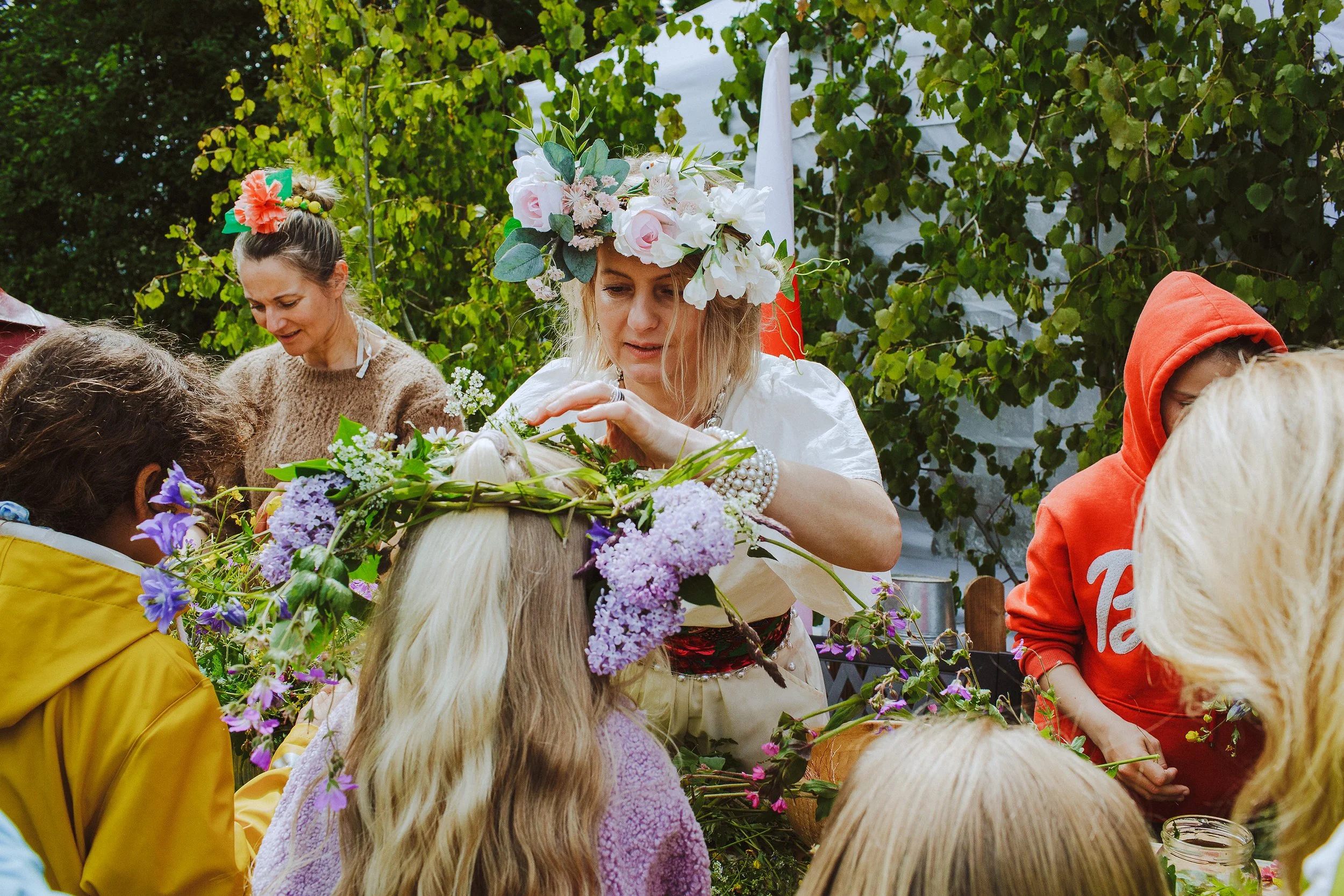 Stoppested Verden internasjonal barnefestival. Kvinne med blomsterkrans lager blomsterkrans til en jente.