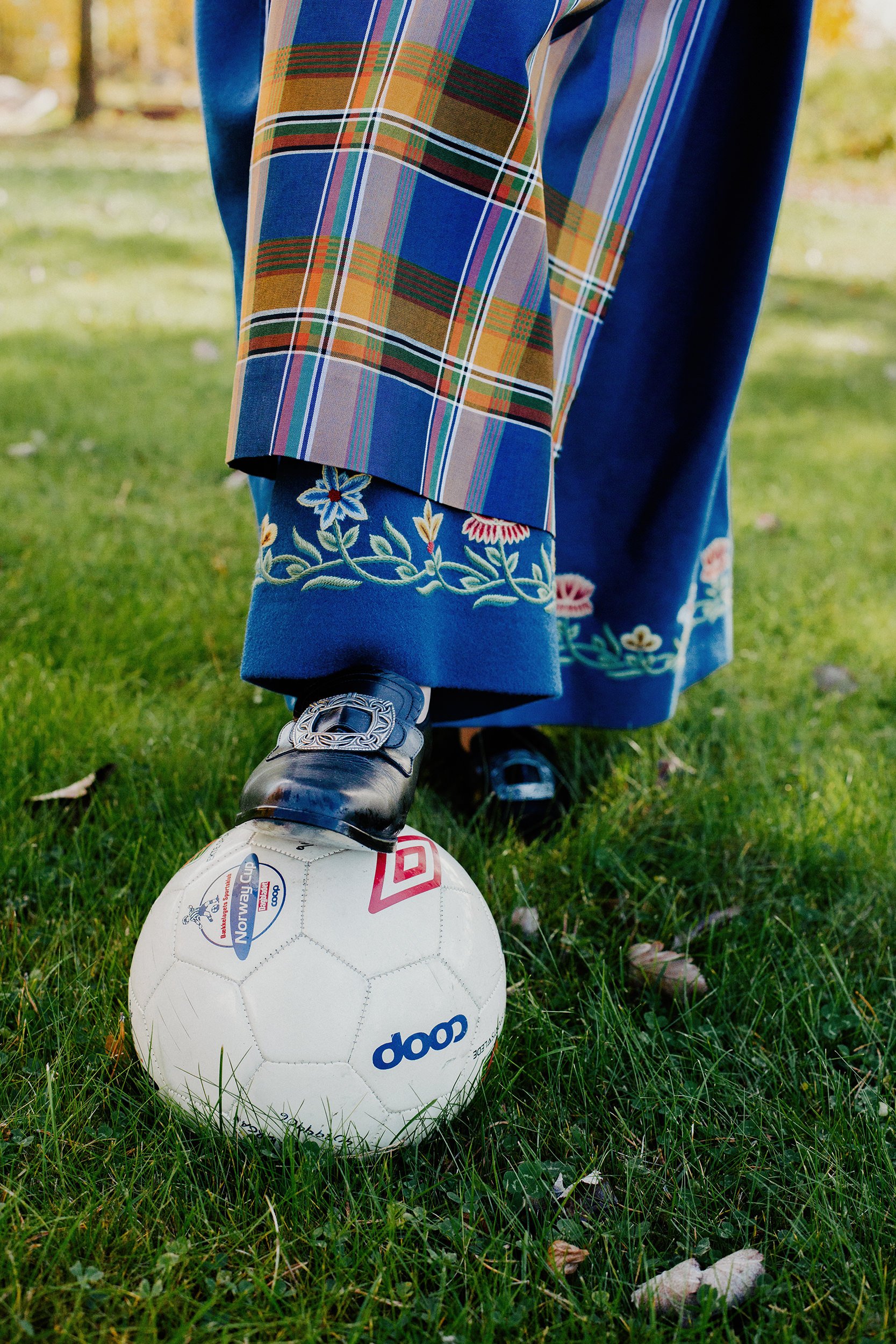 Konfirmantfotografering. Jente med bunad holder foten på en fotball.