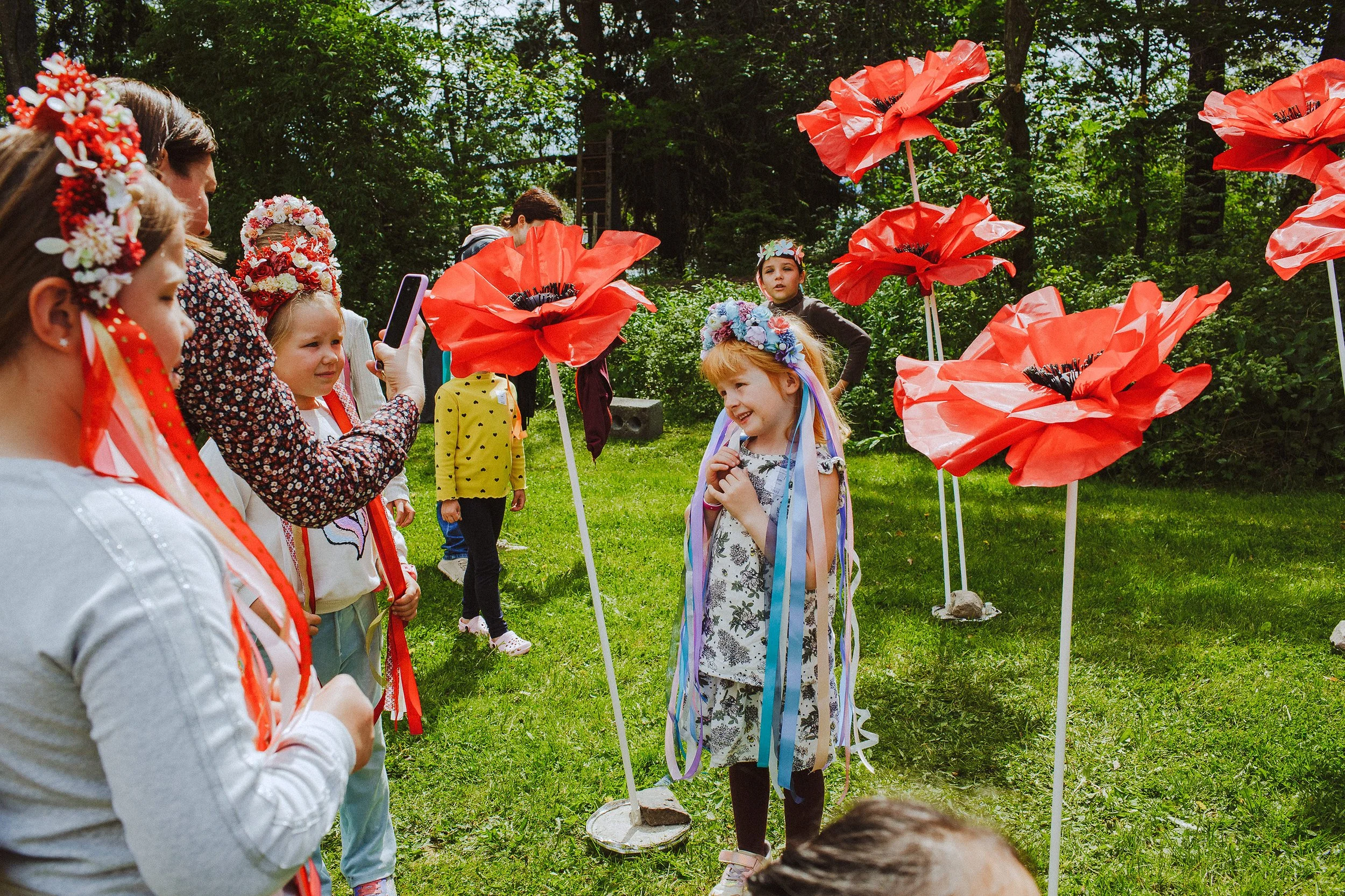 Stoppested Verden internasjonal barnefestival. Jente poserer blant store papirblomster med en blomsterkrans på hodet.