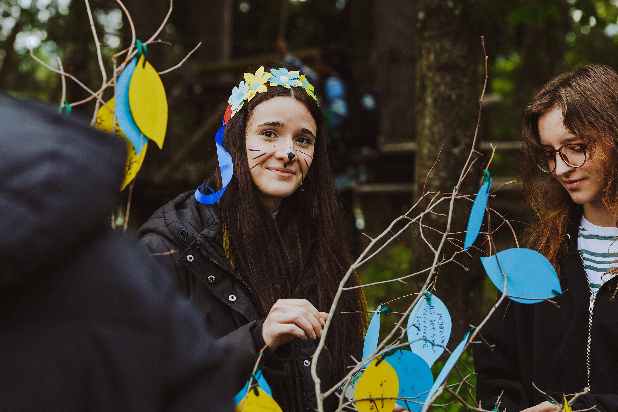Stoppested Verden internasjonal barnefestival. Jente fester lapper i ukrainske farger på en kvist.