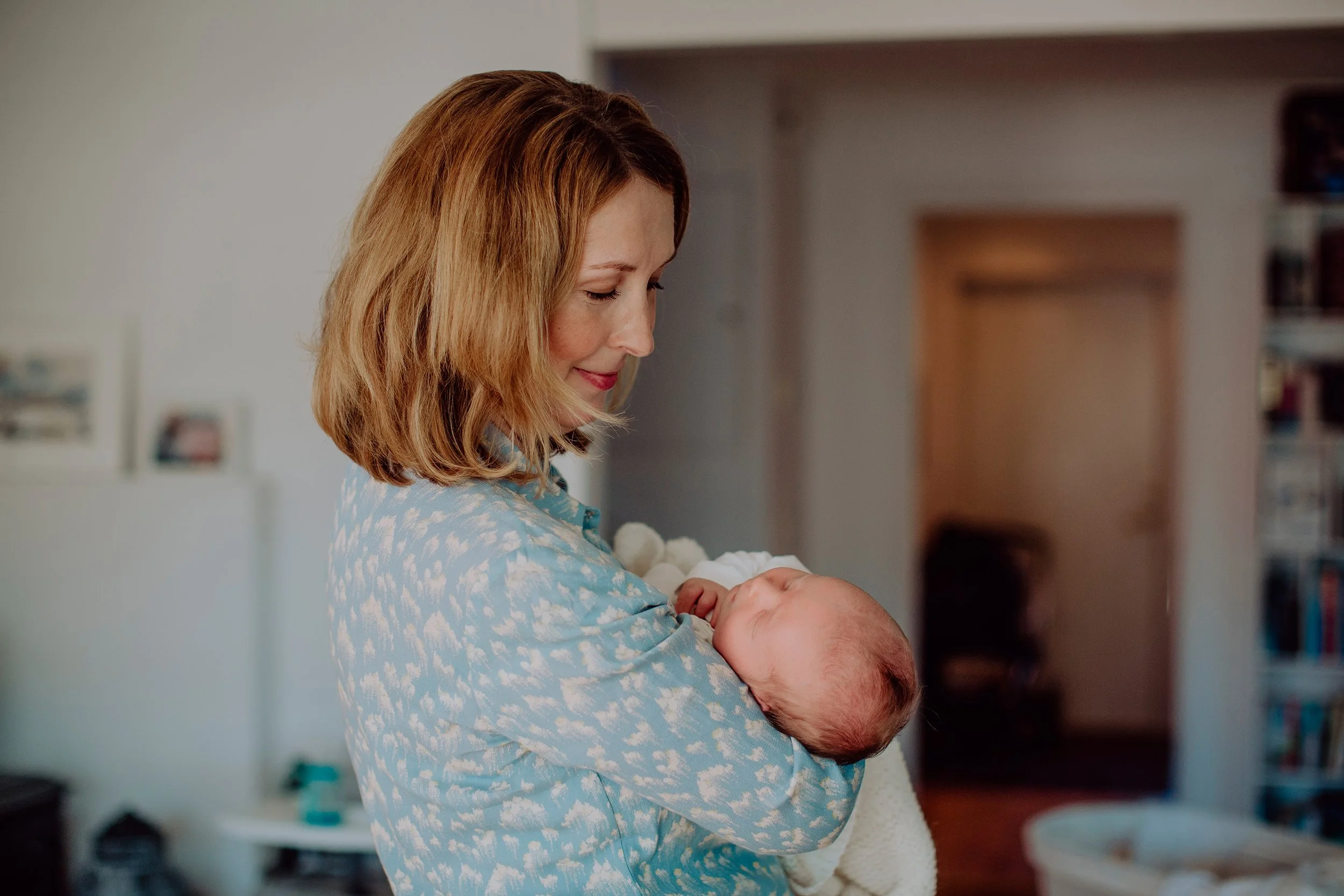 Nyfødtfotografering hjemme. Mor holder nyfødt i armene.