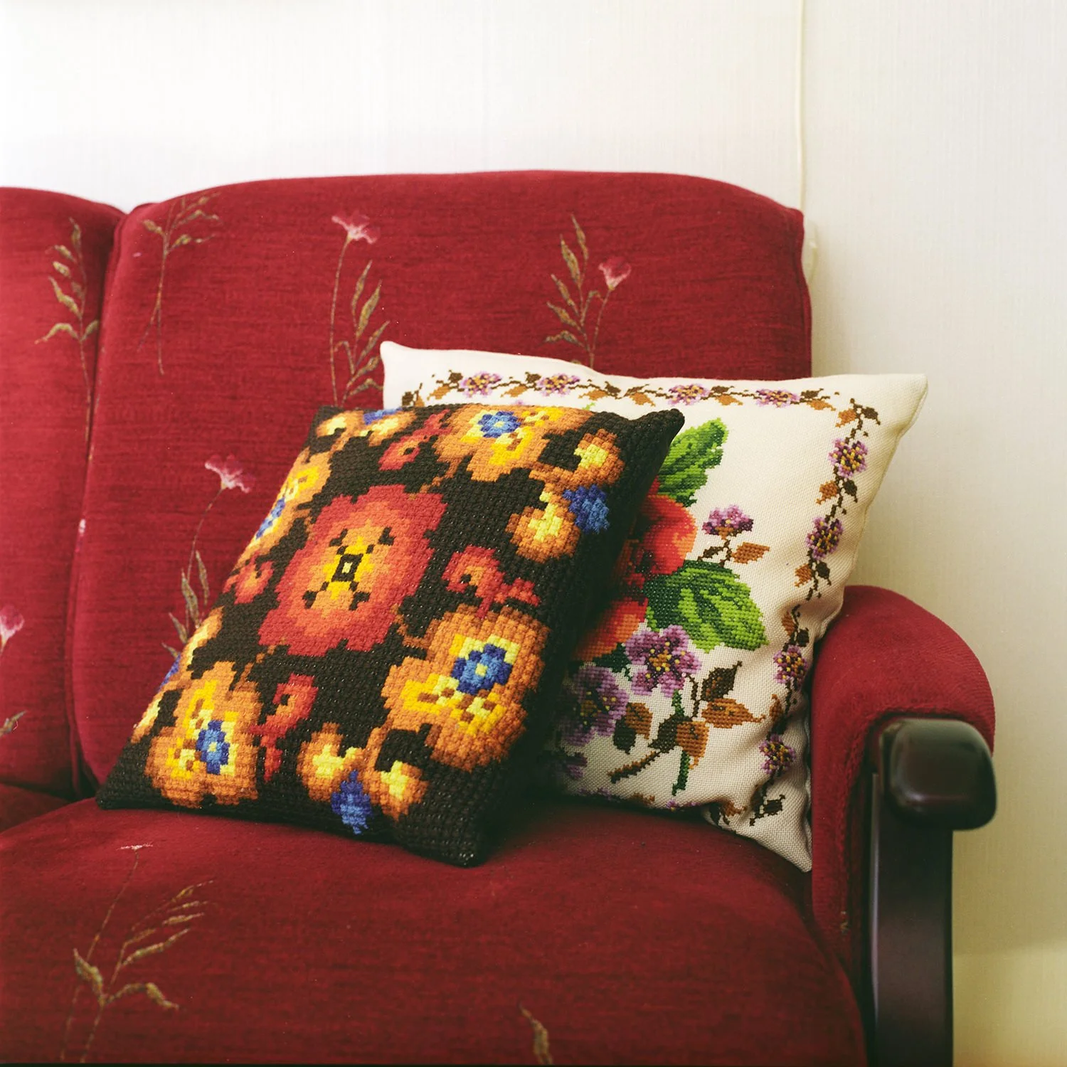 Utsnitt av interiør. To broderte puter på en rød sofa.