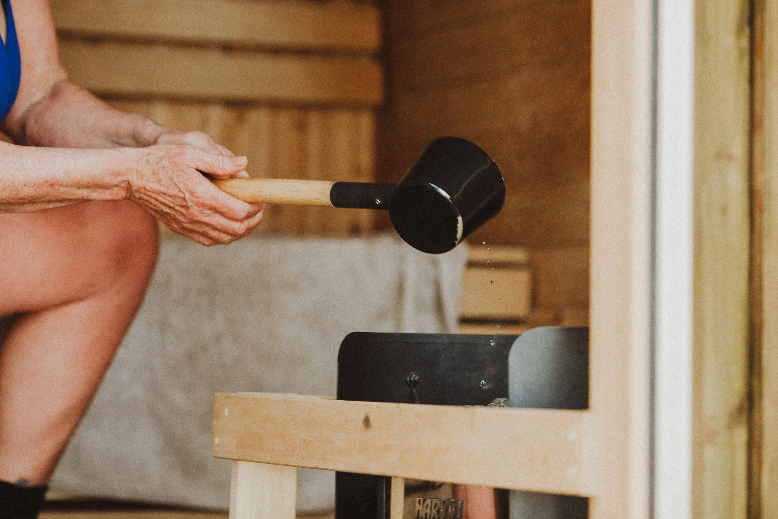 Kvinne øser vann i vedfyrt badstue.