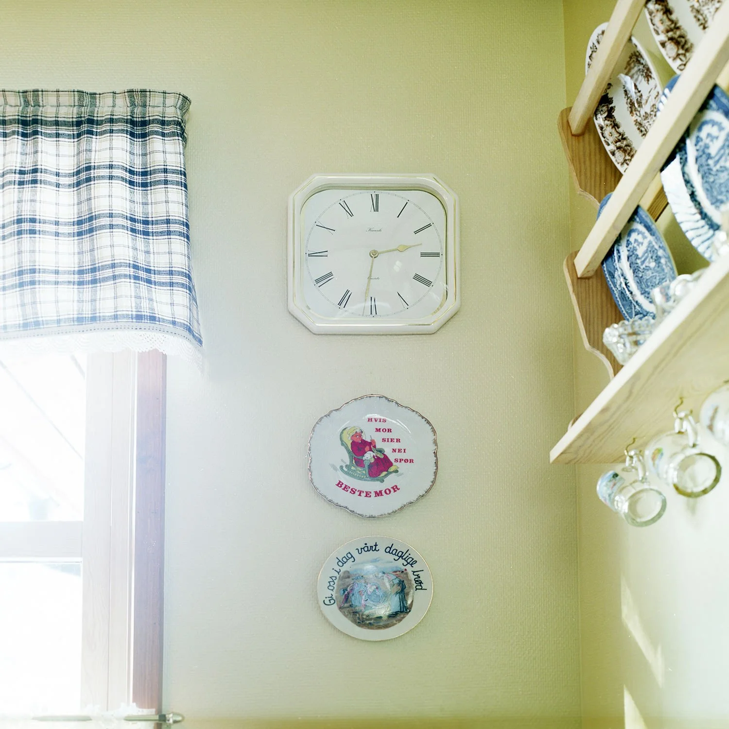 Utsnitt av interiør. Gul vegg med klokke og to pyntetallerkener.