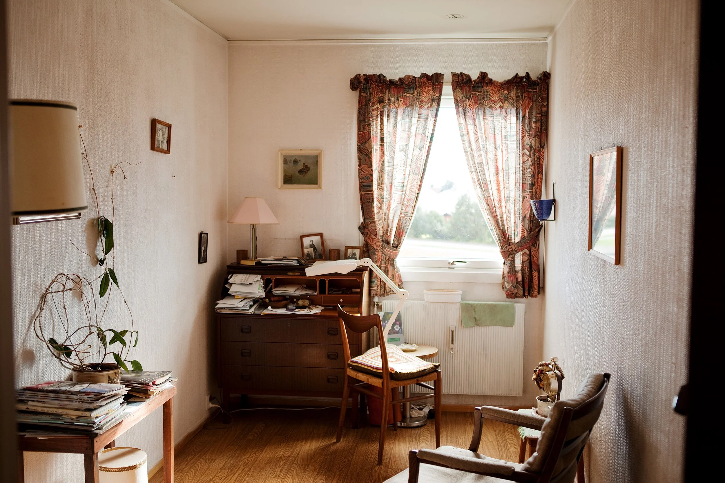 Et rom tilhørende en eldre dame. En stol er plassert foran vinduet.