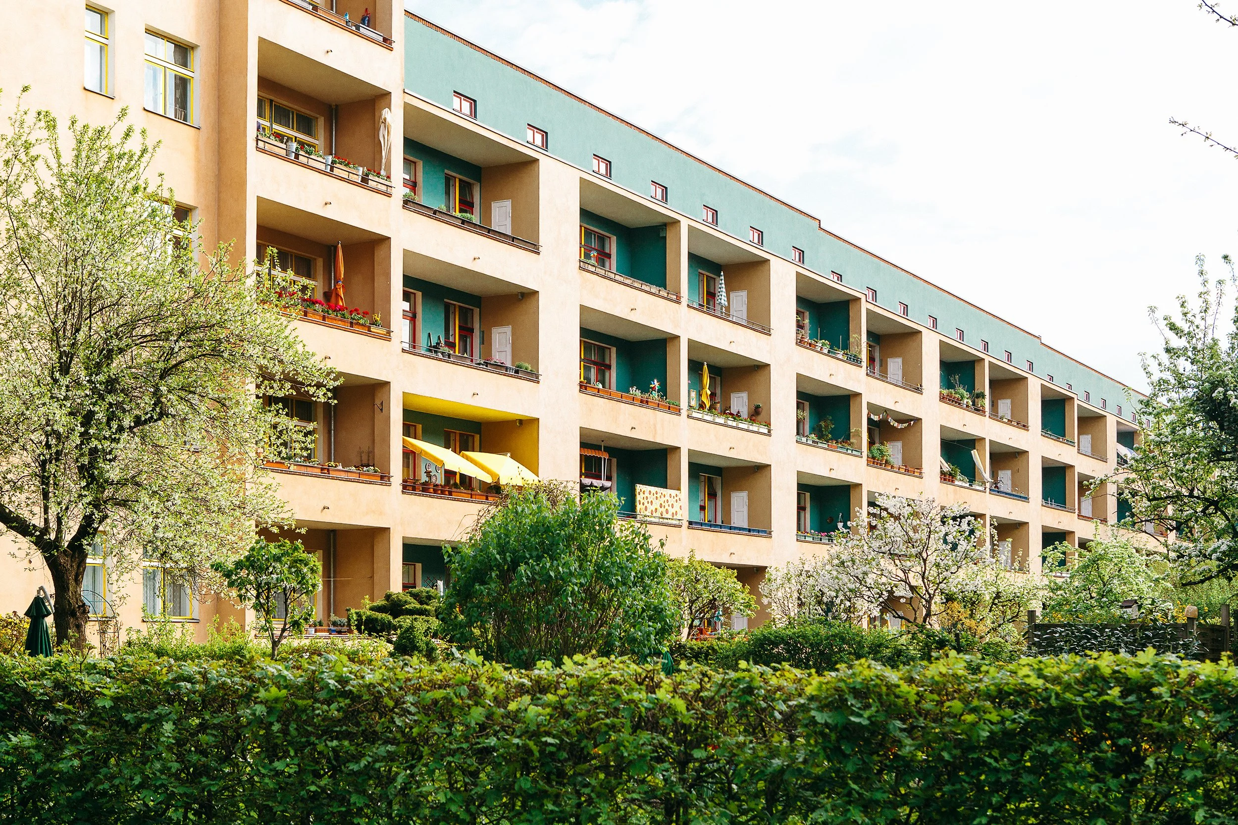 Boligblokk tegnet av Bruno Taut i Berlin. Mange rekker med balkonger. I front er det en frodig og vårlig hage.