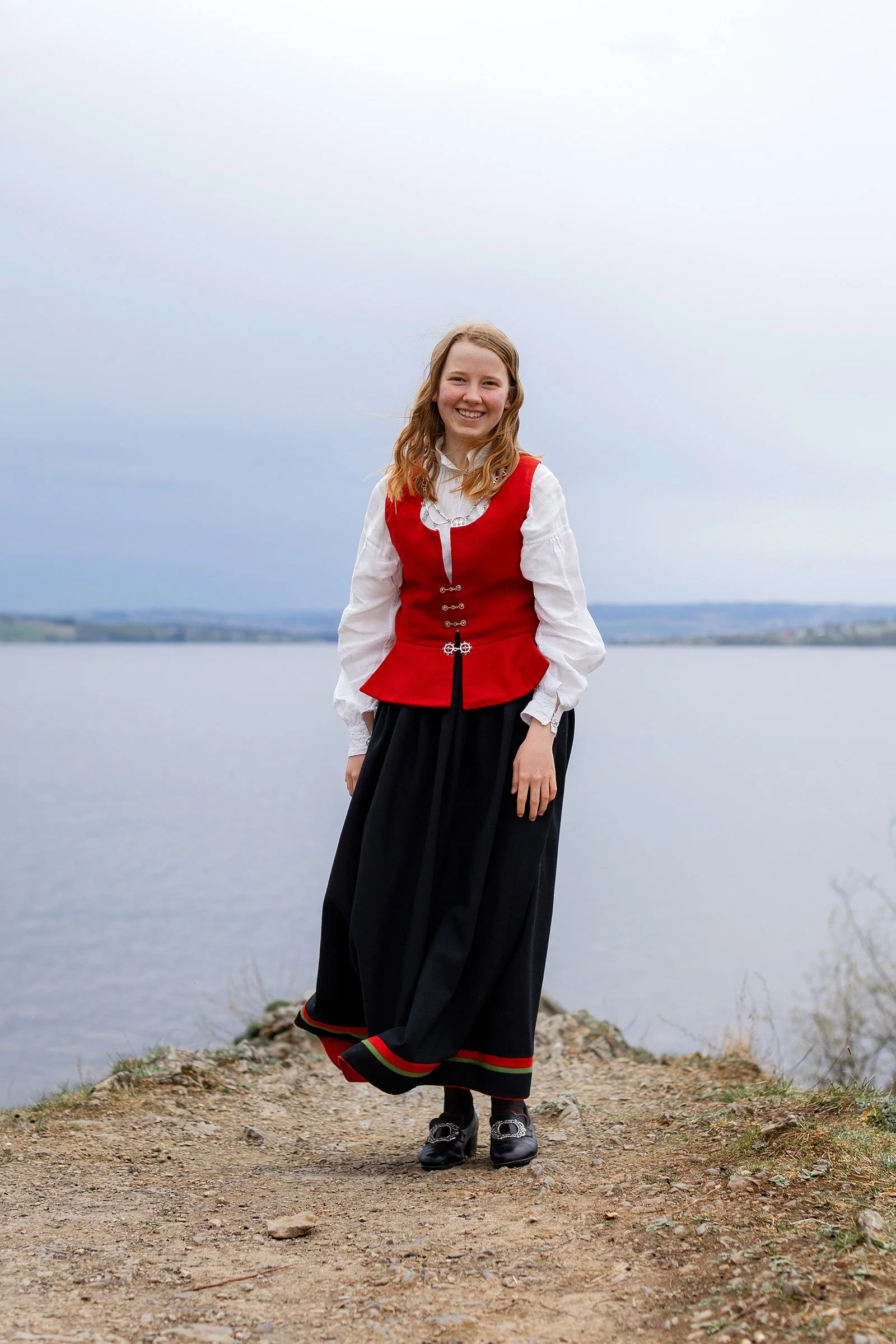 Smilende konfirmant i bunad på toppen av Geitryggen ved Mjøsa i Hamar.