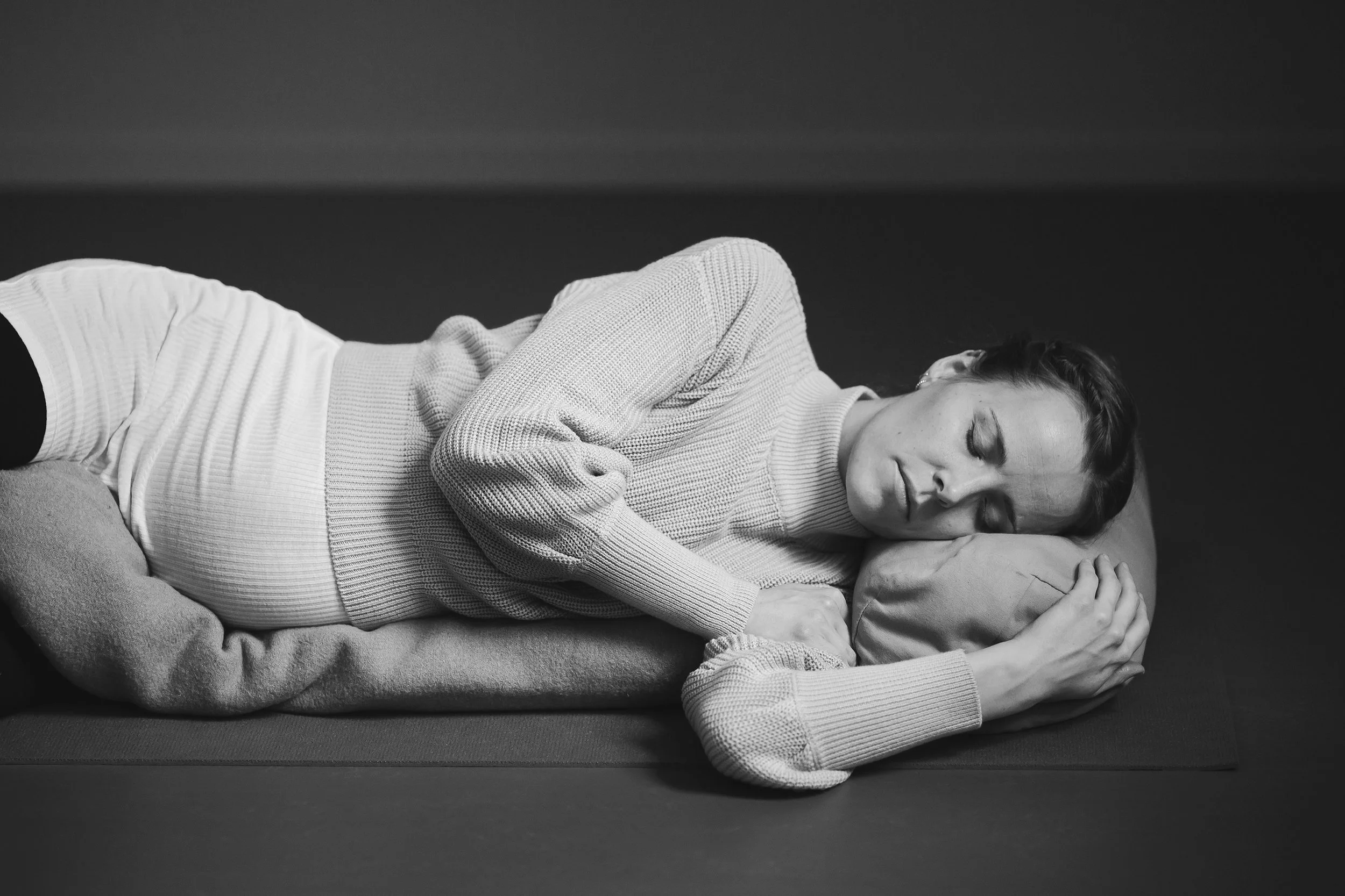 Miljøportrett av gravid kvinne som gjør avslappende yoga på gulvet.