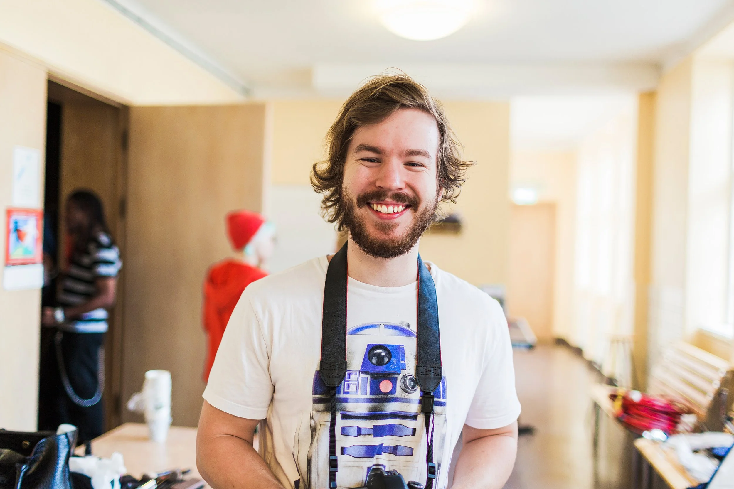 Smilende student går rundt med kamera rundt halsen og dokumenterer.