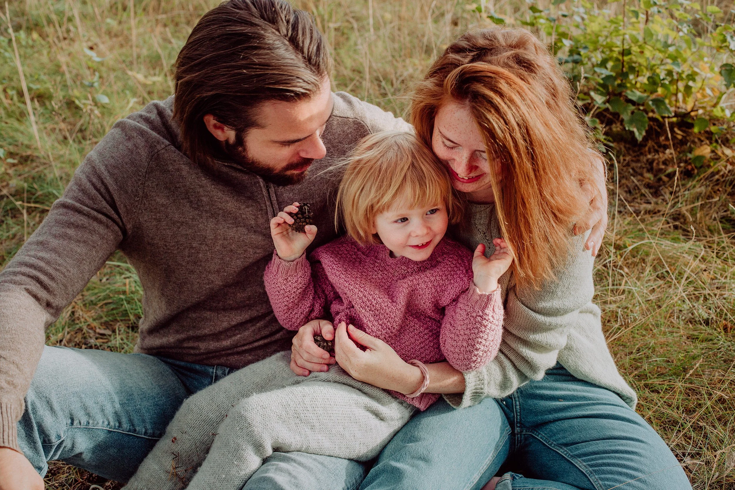 Familiefotografering utendørs i naturlig lys. Familie på tre med to voksne og ett barn