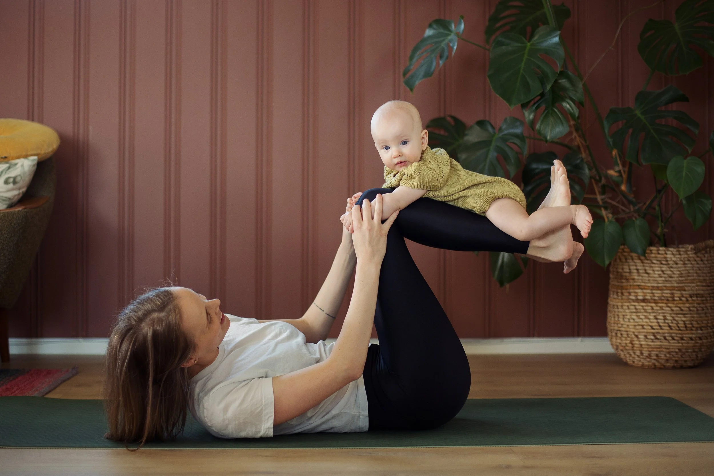 Miljøbilde av mor og baby som gjør yoga sammen på stuegulvet.