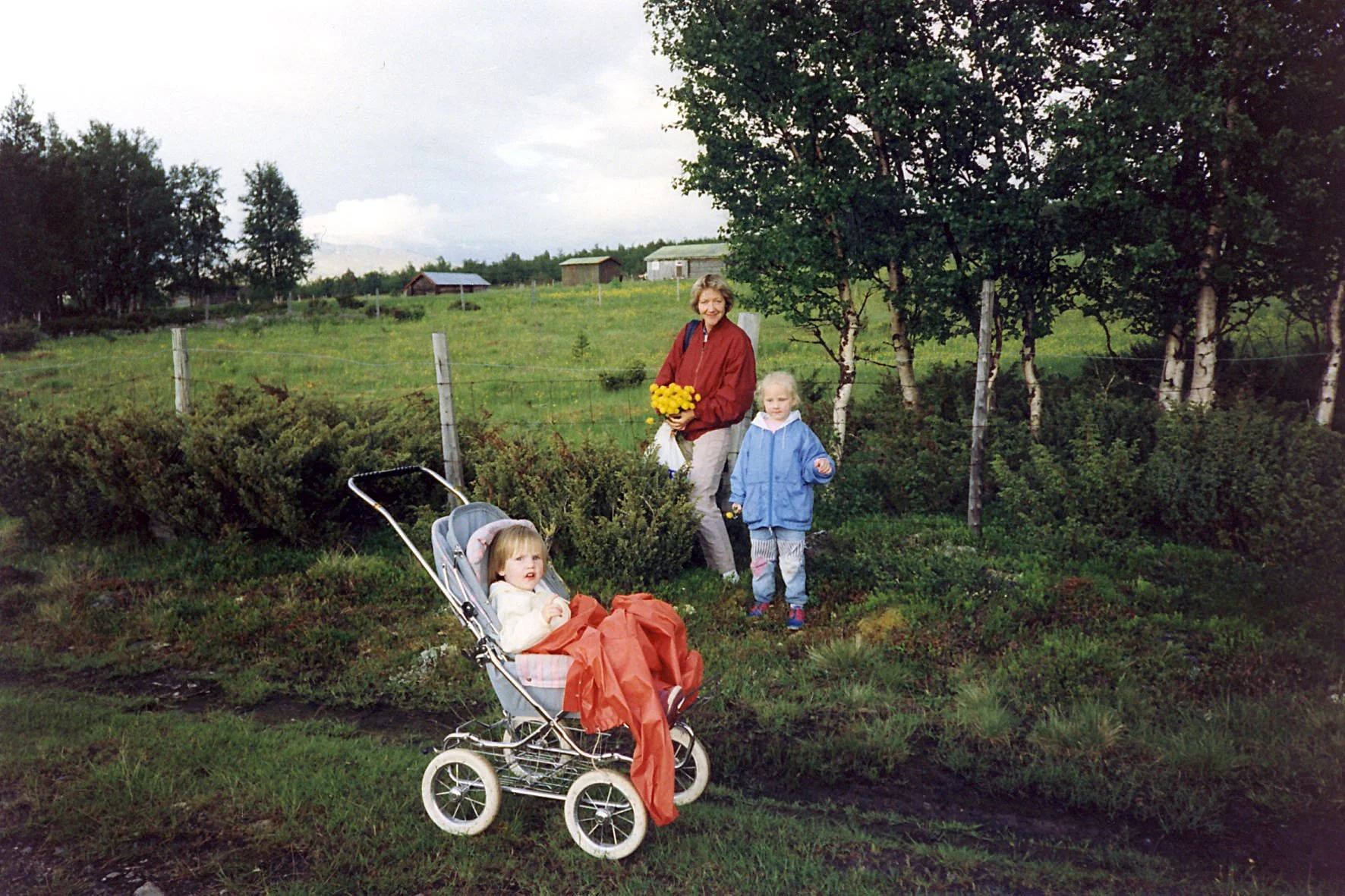 Digitalisert foto av mor med to barn som plukker blomster ved en seter på fjellet.